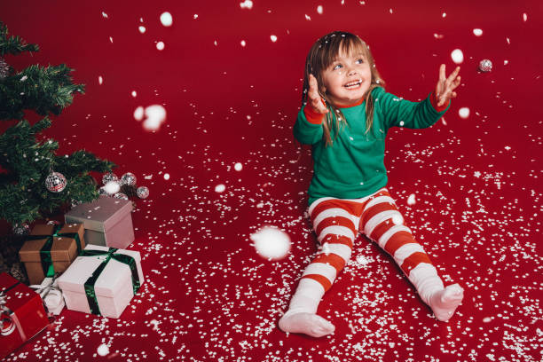 istock Kid sitting beside a christmas tree enjoying artificial snowfall 1063301400