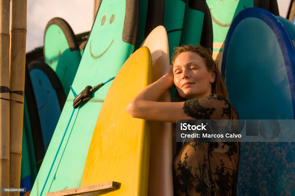 head and shoulders portrait of young beautiful and happy blond woman smiling relaxed and cheerful posing with colorful surf boards in the background in beauty fashion and summer holidays concept head and shoulders portrait of young beautiful and happy blond woman smiling relaxed and cheerful posing with colorful surf boards leaning in surfboard in beauty fashion summer concept 30-39 Years Stock Photo