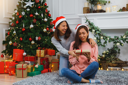 Young Asian woman in sweater gives Christmas gift surprise to friend, Christmas holiday concept