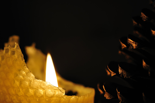 burning candle made of honeycomb beside golden sprayed large pine cone