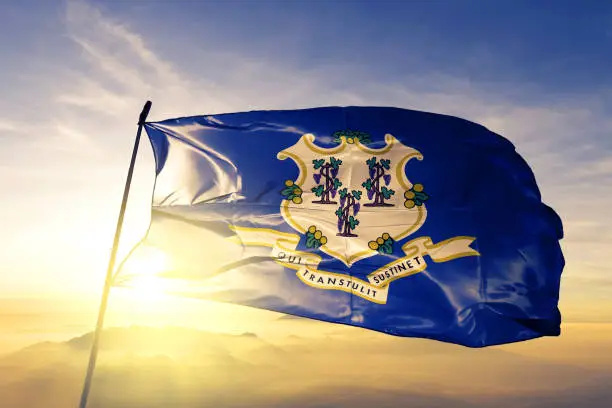 Connecticut state of United States flag on flagpole textile cloth fabric waving on the top sunrise mist fog