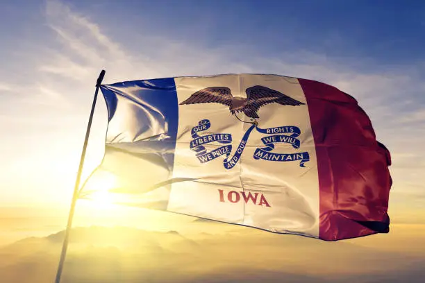 Iowa state of United States flag on flagpole textile cloth fabric waving on the top sunrise mist fog