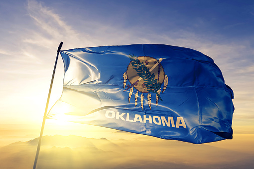 Oklahoma state of United States flag on flagpole textile cloth fabric waving on the top sunrise mist fog