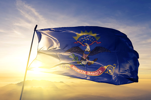 North Dakota state of United States flag on flagpole textile cloth fabric waving on the top sunrise mist fog