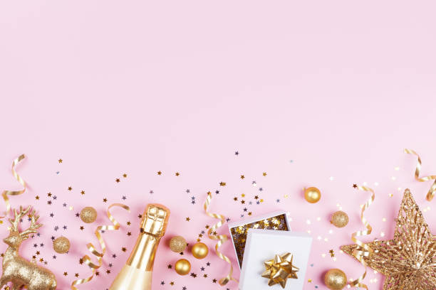 istock Christmas background with golden gift or present box, champagne and holiday decorations on pink pastel table top view. 1063366708