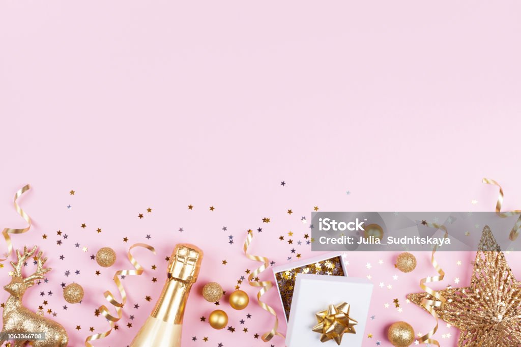 Christmas background with golden gift or present box, champagne and holiday decorations on pink pastel table top view. Christmas background with golden gift or present box, champagne and holiday decorations on pink pastel table top view. Greeting card. Flat lay style. New Year Stock Photo