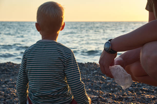 Father and son clean the garbage and take care of the environment on the beach at sunset stock photo