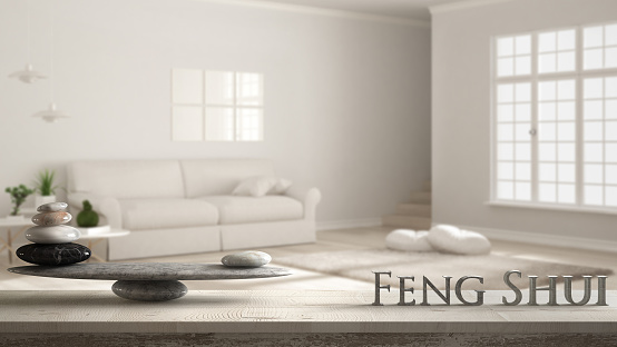 Wooden vintage table shelf with stone balance and 3d letters making the word feng shui over scandinavian living room with sofa and carpet fur, zen concept interior design
