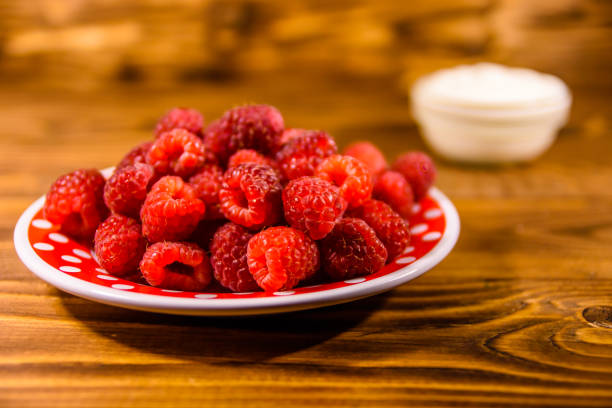 istock Ceramic plate with ripe raspberries and sour cream on wooden table 1063388154
