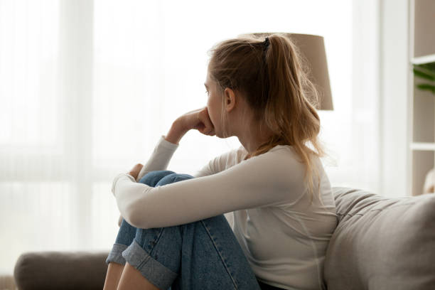 malestar mujer sentada en sofá solo en casa - tristeza fotografías e imágenes de stock