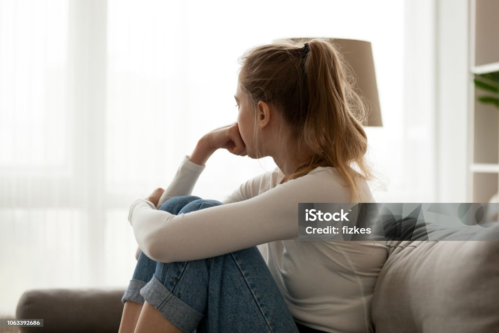 Upset woman sitting on couch alone at home Side view young woman looking away at window sitting on couch at home. Frustrated confused female feels unhappy problem in personal life quarrel break up with boyfriend or unexpected pregnancy concept Women Stock Photo