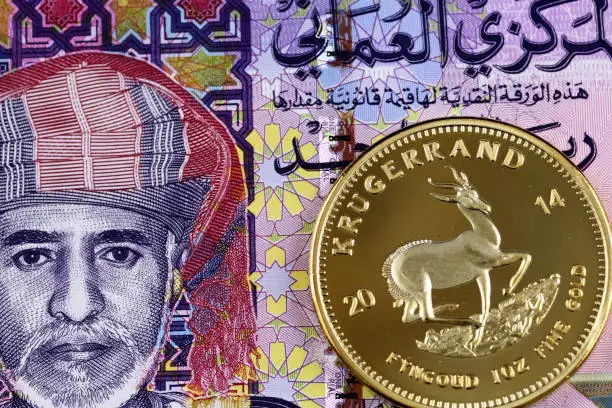 A close up image of a colorful Omani one rial bank note with a gold krugerrand coin