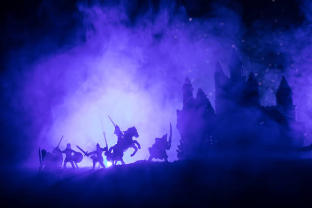 istock Medieval battle scene with cavalry and infantry. Silhouettes of figures as separate objects, fight between warriors on dark toned foggy background with medieval castle. Night scene. Selective focus 1063424530