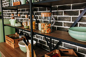 Black loft style storage stand with ceramic and wooden dishware in kitchen. Brick wall background