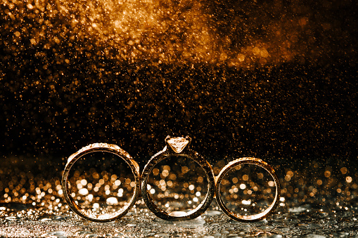 Three golden wedding engagement rings isolated on dark background with water fog yellow effect.