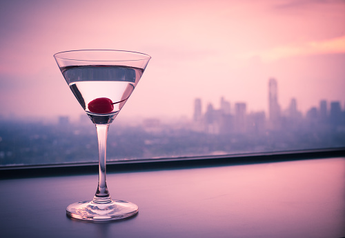 Glass of martini standing next to the window with city view.