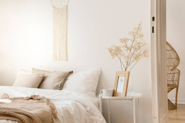 istock Bedside table with mug and framed picture next to comfortable king size bed with linen bedding and beige blanket, real photo 1063498920