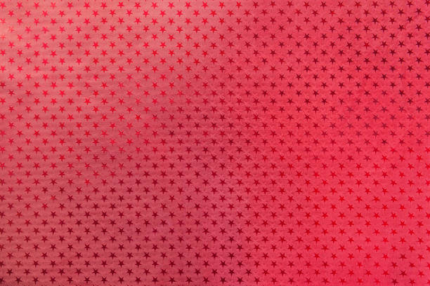 Red background from metal foil paper with a pattern of sparkling stars closeup. Texture of metallized wrapping holiday paper surface.