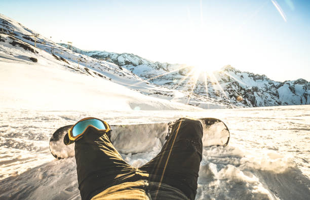 snowboarder sitting at sunset on relax moment in european alps ski resort - winter sport concept with guy and snowboard on mountain top ready to ride - legs point of view on vintage contrast filter - slalom skiing imagens e fotografias de stock