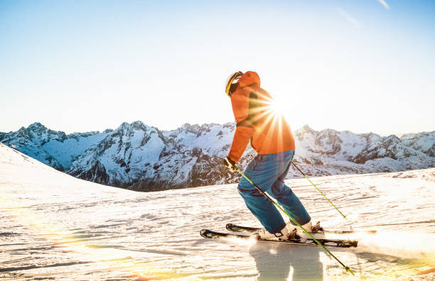 Professional skier athlete skiing at sunset on top of french alps ski resort - Winter vacation and sport concept with adventure guy on mountain top riding down the slope - Warm bright sunshine filter stock photo