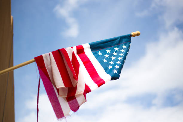 istock Tattered Old US Flag Hanging; Sky Background 1063553860