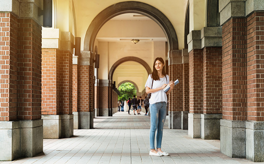 A student holding books standing in the cornor of campus