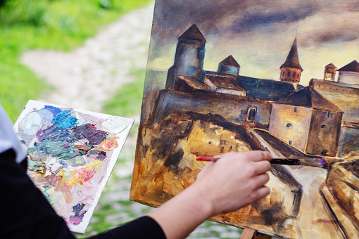 Student artist paints painting paint and brush. The picture depicts an old fortress in the city of Kamyanets-Podilsky. Work artist.