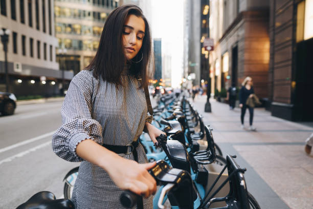 chica alquila una bici de la ciudad desde un punto de sujeción - bikeshare fotografías e imágenes de stock