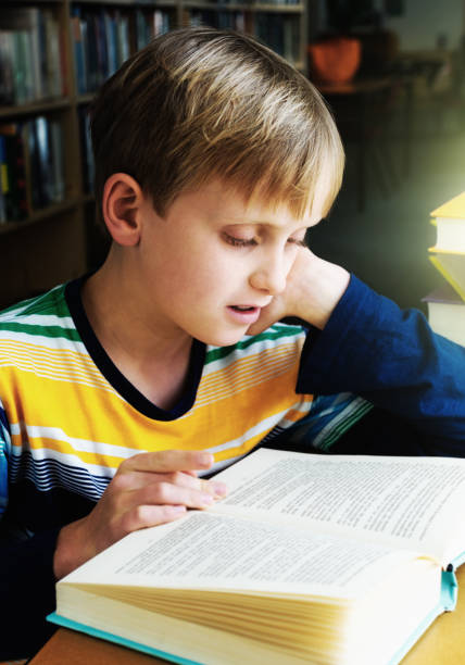 istock Little boy reading book in library looks down, absorbed 1063611172