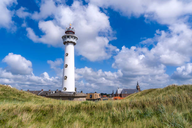 White lighthouse in the dunes with churches and houses of a little village in the background under a beautiful sky