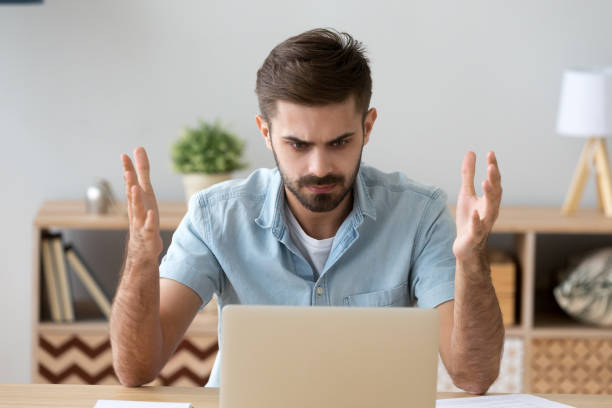 istock Irritated man looking at laptop screen sitting at the desk 1063637526