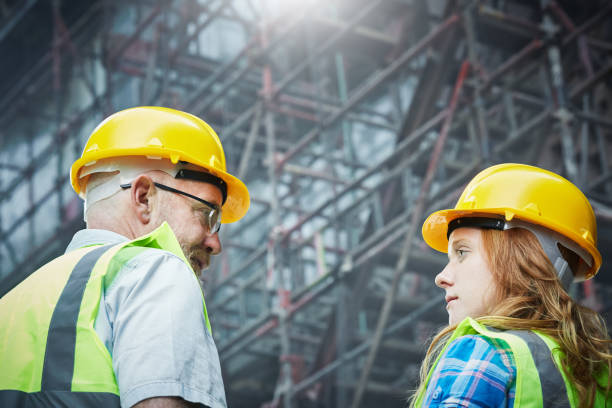istock Mature male  construction worker talking to female trainee beneath scaffolding 1063637826