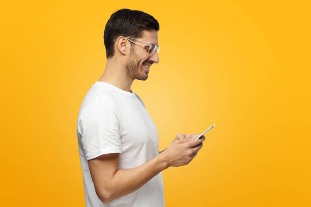 istock Young attractive man looking and at smartphone while texting, using mobile phone, isolated on yellow background 1063638616