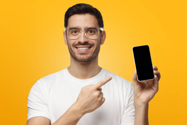 istock Handsome man showing smartphone and pointing with finger at blank screen with copy space, isolated on yellow background 1063638626