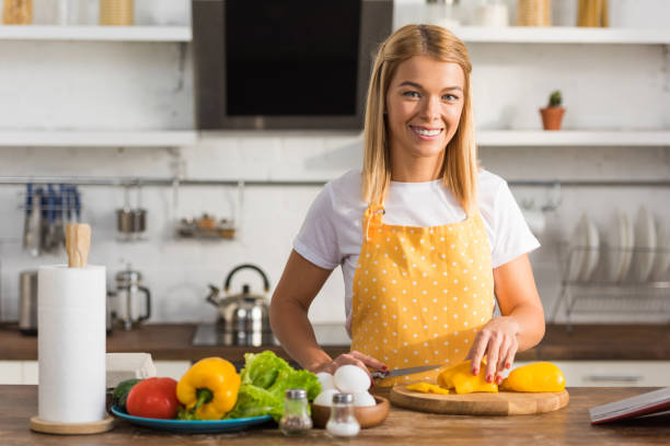 istock happy young woman cutting vegetables and smiling at camera in kitchen 1063647216