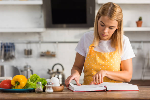 istock young woman in apron reading cookbook while cooking in kitchen 1063648646