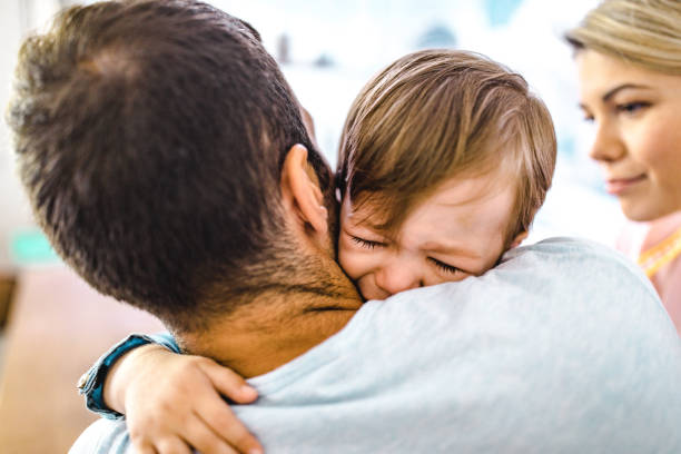 Little boy crying in his father's embrace at home.