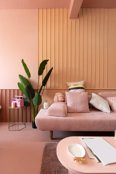 Cozy living room corner with pink sofa covered with comfprtable pink pillows on decorated wall background feature and artificial plant on the left side / cozy interior concept / decoration idea