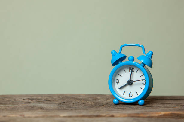 istock Blue alarm clock on a gray background and wooden table. Copy space for text 1063657318