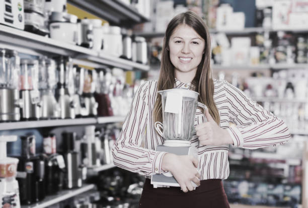 Smiling girl seller showing liquidiser in shop Smiling girl seller showing liquidiser in domestic appliances section liquidiser stock pictures, royalty-free photos & images