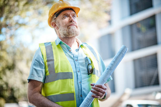 istock Mature male construction worker looks up, concentrating, holding blueprints 1063668132