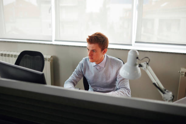 Young businessman working in the office, sitting by the desk and using computer.