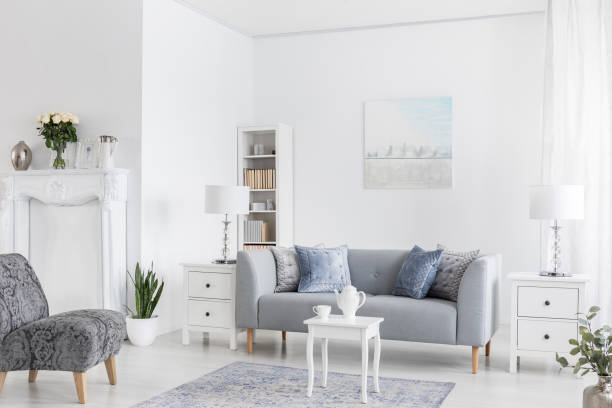 istock Grey sofa between white cabinets with lamps in flat interior with armchairs and table on carpet. Real photo 1063674822