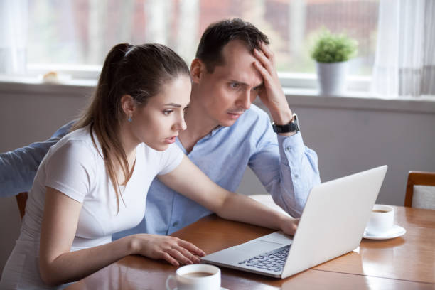 jeune couple déçu courriel obtenir de mauvaises nouvelles sur ordinateur portable - women computer couple surprise photos et images de collection