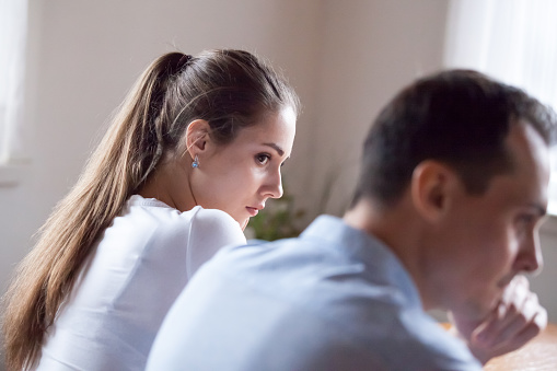 Back view of offended woman looking at stubborn lover refusing reconcile after fight, mad millennial couple not talking after quarrel, man avoid looking or speaking to female after family conflict