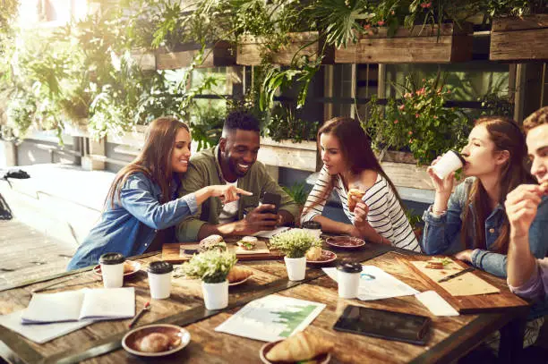 Shot of three friends looking at something on a cellphone while out for lunch