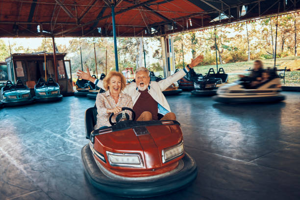 enjoying retirement playful senior couple having fun together driving bumper car bizarre stock pictures, royalty-free photos & images