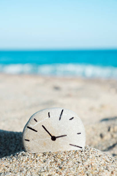 istock clock drawn on a stone, on the sand of a beach 1063690706