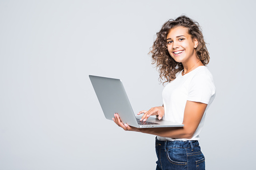 Young mixed race positive cool woman with curly hair using laptop and smiling isolated over white background