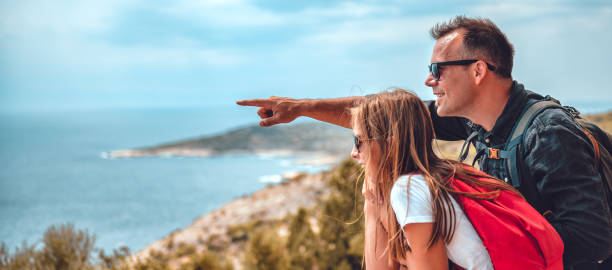 istock Father and daughter sitting on cliff's edge by the sea 1063697988